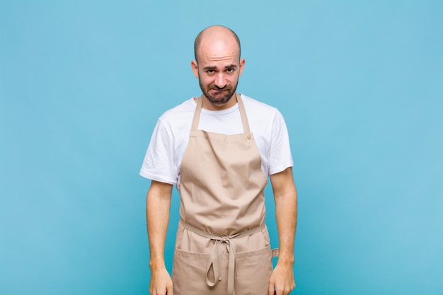 Bald man looking puzzled and confused, biting lip with a nervous gesture, not knowing the answer to the problem