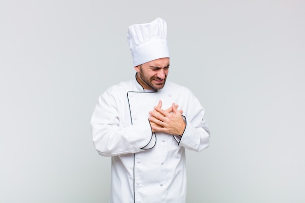 Bald man looking sad, hurt and heartbroken, holding both hands close to heart, crying and feeling depressed