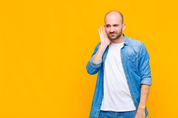 Bald man looking serious and curious, listening, trying to hear a secret conversation or gossip, eavesdropping