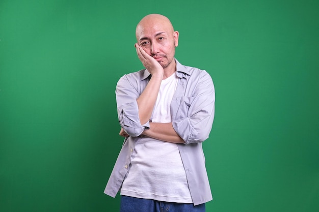 Bald man looking tired and bored with depression problems against green background