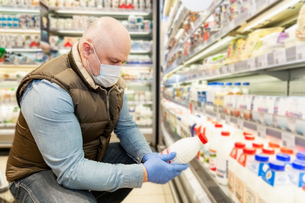 Un uomo calvo con una mascherina medica sceglie i latticini in un supermercato. una corretta alimentazione e uno stile di vita sano. autoisolamento durante la pandemia di coronavirus. avvicinamento.