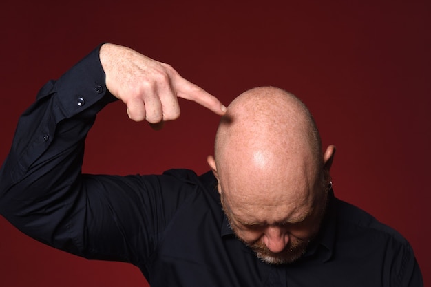 Foto uomo calvo che punta la testa su sfondo rosso