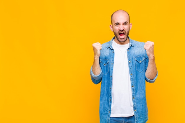 Bald man shouting aggressively with an angry expression or with fists clenched celebrating success