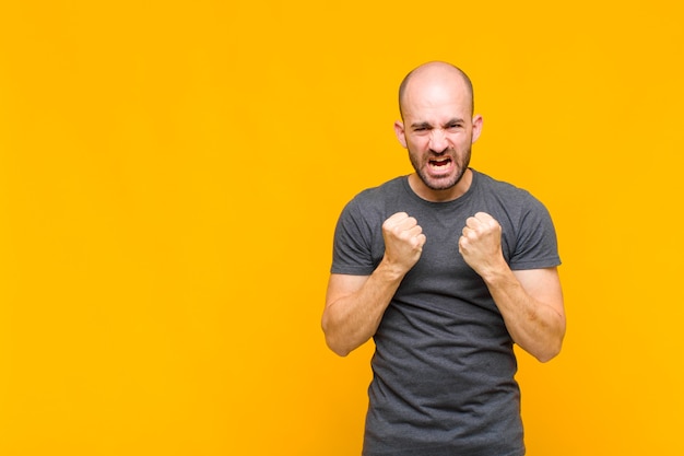 Bald man shouting aggressively with annoyed, frustrated, angry look and tight fists, feeling furious