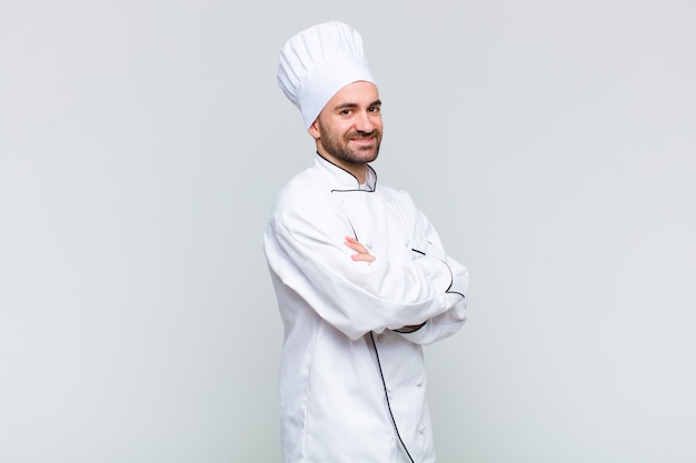 Bald man smiling to camera with crossed arms and a happy, confident, satisfied expression, lateral view