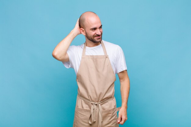 Bald man smiling cheerfully and casually, taking hand to head with a positive, happy and confident look