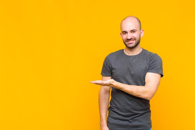 Bald man smiling cheerfully, feeling happy and showing a concept in copy space with palm of hand