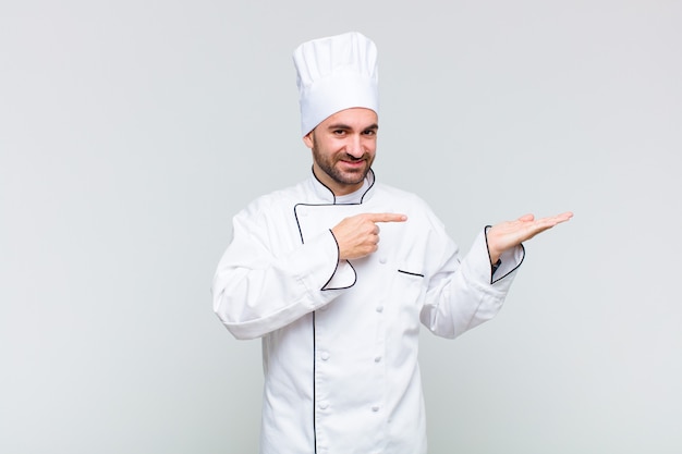 Bald man smiling, feeling happy, carefree and satisfied, pointing to concept or idea on copy space on the side