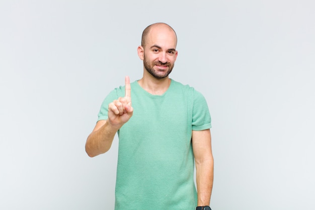 Bald man smiling and looking friendly, showing number one