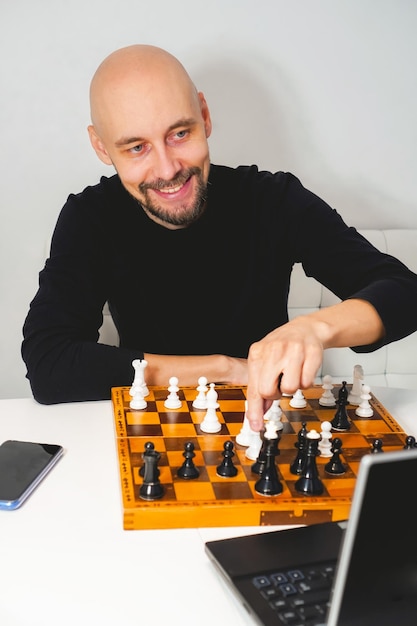 Bald man wearing beard playing chess on board near laptop\
strategy and competition concept