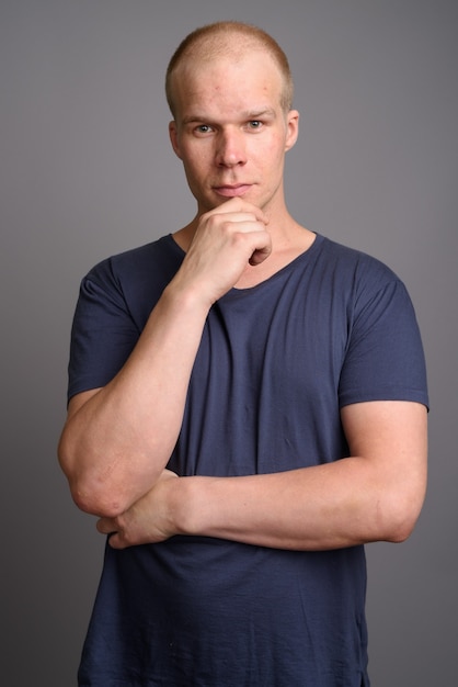 Bald man wearing blue shirt against gray wall