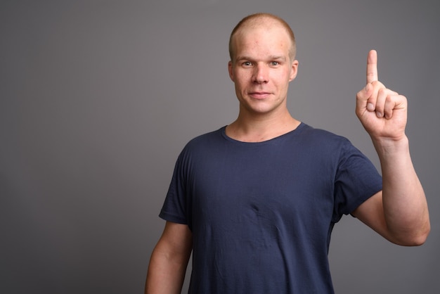 Bald man wearing blue shirt against gray wall