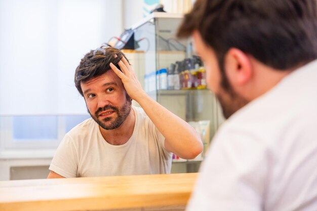 Photo bald man with capillary prosthesis looking into hair salon mirror