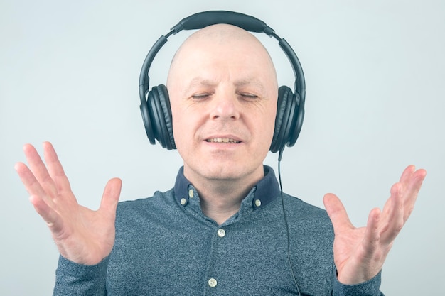 Bald man with closed eyes listens to music with headphones on a light background