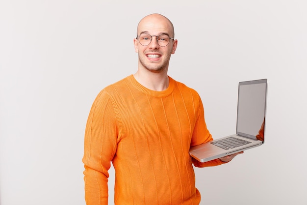 Bald man with computer looking happy and pleasantly surprised, excited with a fascinated and shocked expression