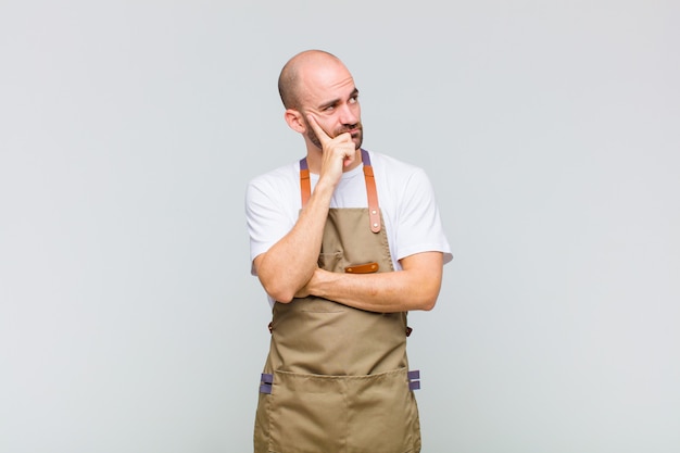 Bald man with a concentrated look, wondering with a doubtful expression, looking up and to the side