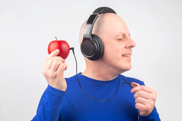 Bald man with headphones listens to music through a red apple player. Metaphor and concept of vitamin benefits in music and sound
