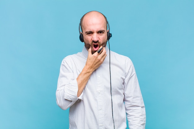 Bald man with mouth and eyes wide open and hand on chin, feeling unpleasantly shocked, saying what or wow