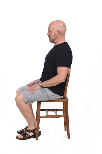 Bald man with sandals t-shirt and shorts sitting on white background, look side