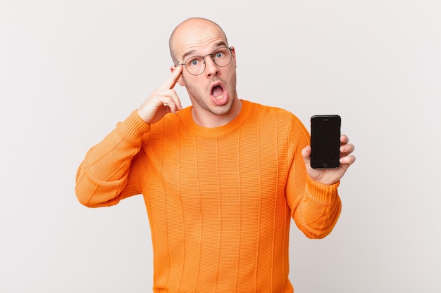 Bald man with a smartphone looking surprised, open-mouthed, shocked, realizing a new thought, idea or concept