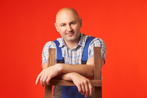 Bald man in a work suit stands with his hands resting on a brown staircase