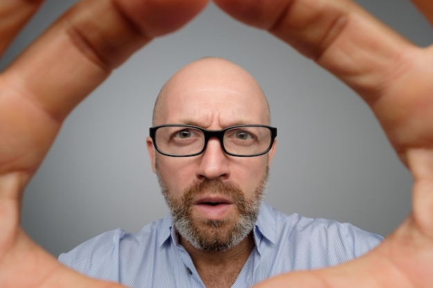 Foto ragazzo maturo calvo in camicia casual grigia che scopre la telecamera nascosta