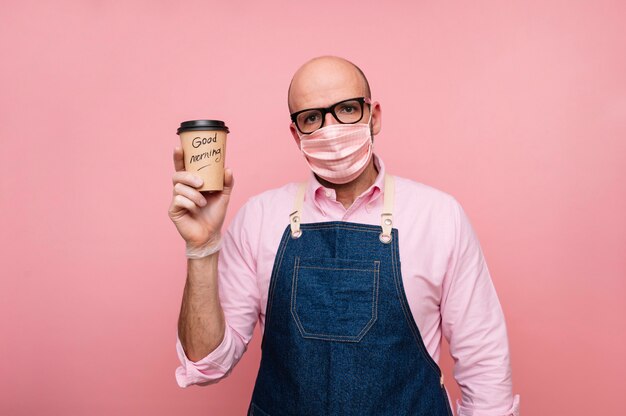 Uomo maturo calvo con maschera e caffè in tazza di cartone riciclabile