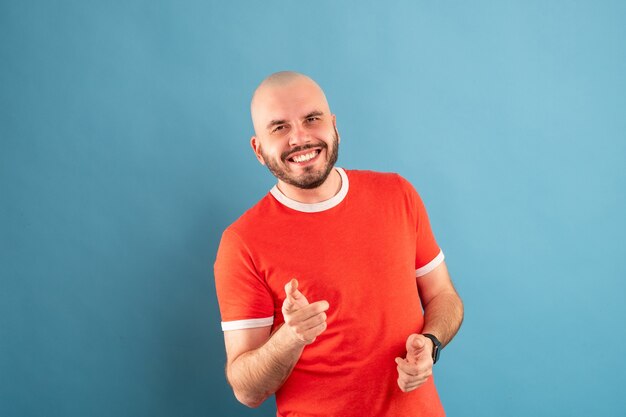 A bald middle-aged man with a beard in a red T-shirt on a blue background stands with his arms shows how simple everything is. Isolated.