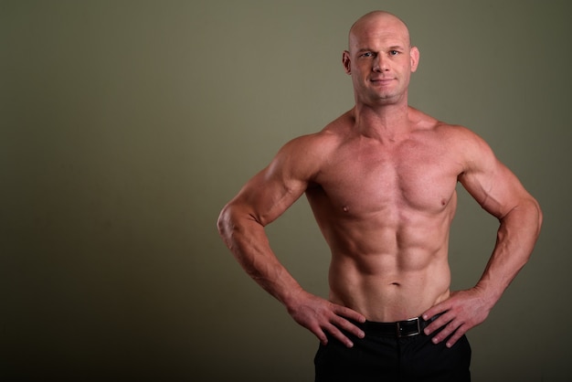 Bald muscular man shirtless against colored wall