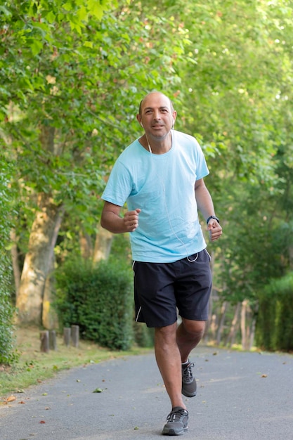 Bald older man running through the park and doing sports to get in shape and slim his belly