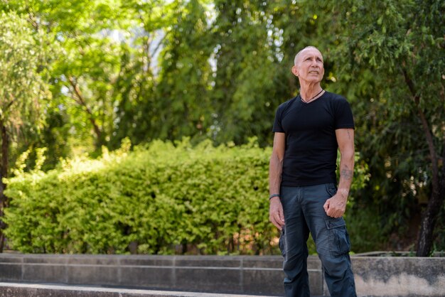 Bald senior tourist man standing and thinking while looking up