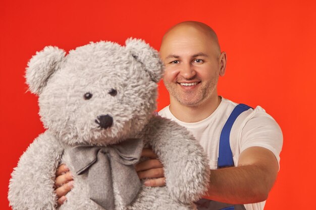 Bald smiling male courier in a work suit hands over a gray teddy bear