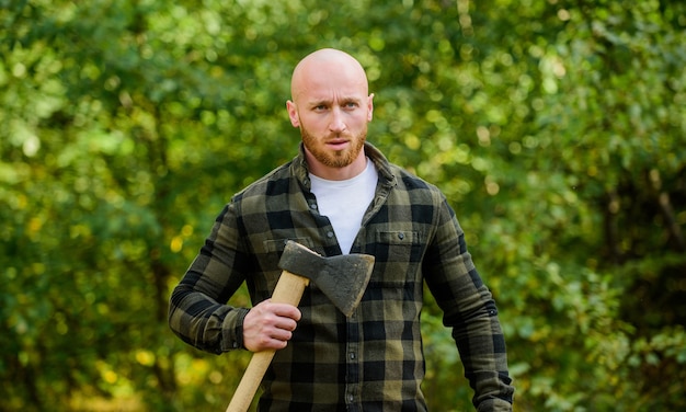 Bald woodsman. Harvest firewood. Hike vacation. Hike in forest. Forest care. Determination of human spirit. Man checkered shirt use axe. Brutal male in forest. Power and strength. Lumberjack carry ax.