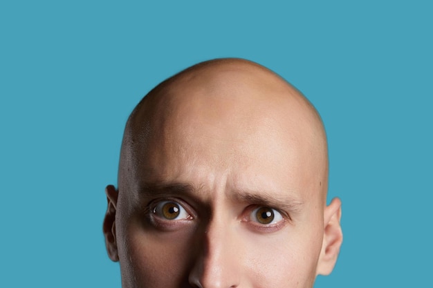 Bald young guy closeup on an empty blue background