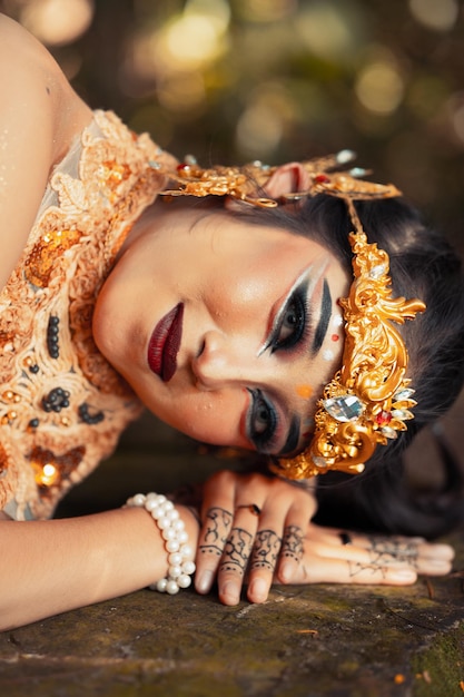 Photo balinese woman with a golden crown and golden necklace sleeping on the rock