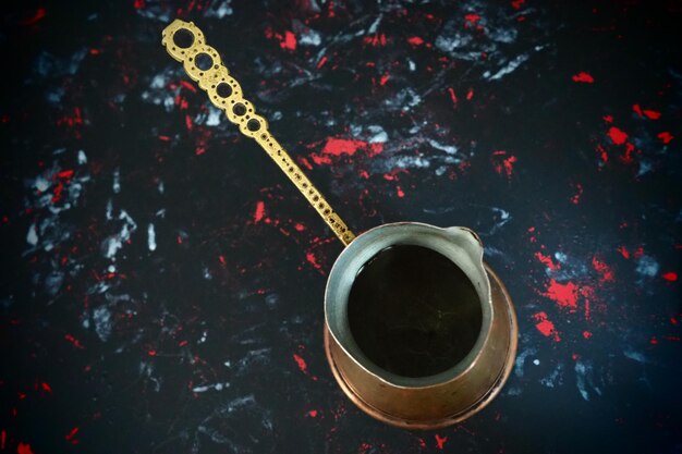터키 커피를 위한 발칸 세즈베 검은색 표면에 있는 구리 세즈베 앤티크 청동 기구 패턴이 있는 금속 손잡이 조각 흰색 빨간색과 파란색 반점이 있는 검은색 배경