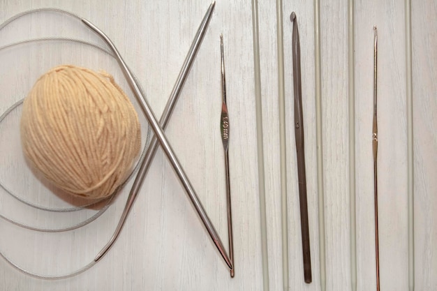 白いテーブルの上にベージュの糸の玉、金属製の編み針。
