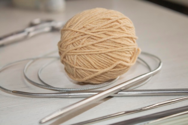 A ball of beige yarn, metal knitting needles on a white table.