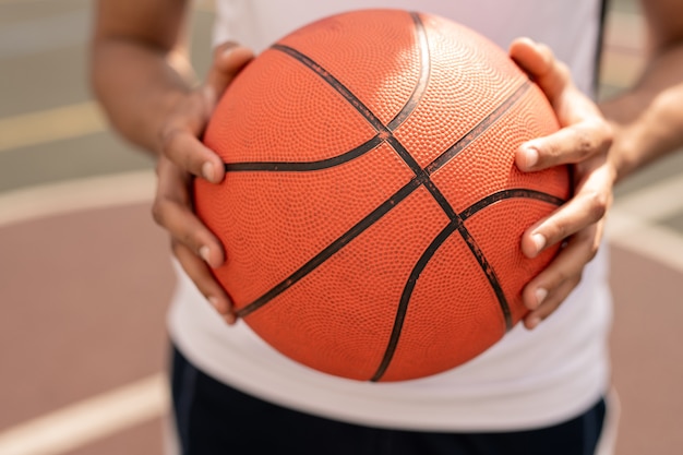 Ball for playing basketball in hands of young active player before throwing it in basket during game