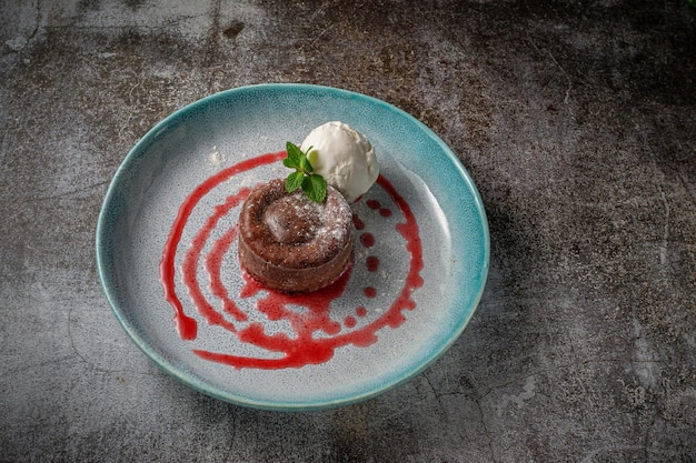 Ballen van chocolade en roomijs met aardbeiensiroop in een blauw bord op een grijze stenen tafel