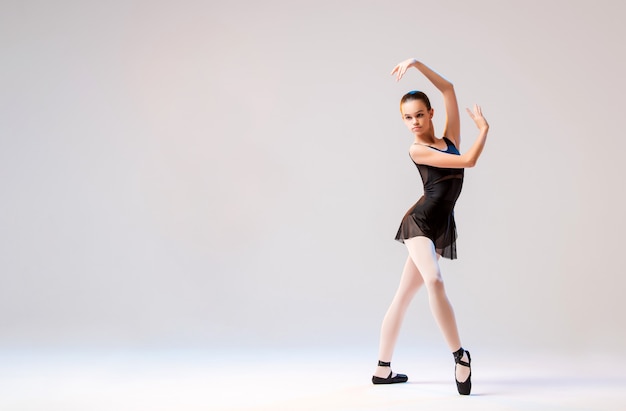 Ballerina in black pointes posing in a graceful pose on a white background