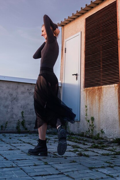 黒いスカートとボディスーツを着たバレリーナが屋根の上を歩き、街の夕日を眺める