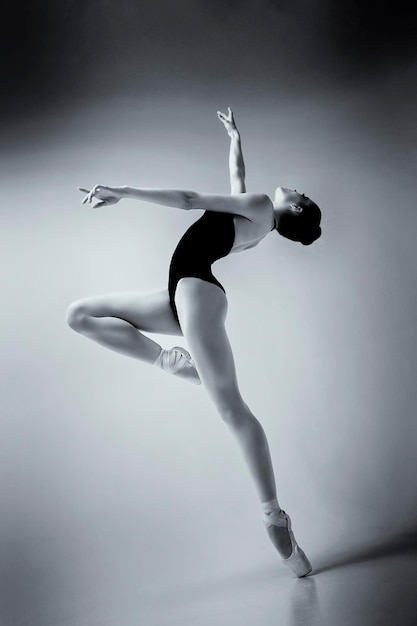 A ballerina in a bodysuit and pointes poses in a photo studio in motion showing beautiful long legs