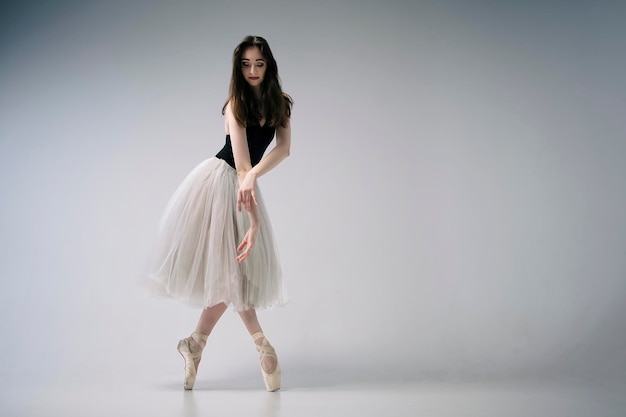 A ballerina in a bodysuit and a white skirt improvises classical and modern choreography in a photo studio