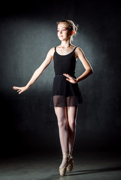 발레리나. 포즈와 스튜디오에서 춤을 귀여운 소녀. 소녀는 발레를 공부하고 있습니다. 어두운 벽.