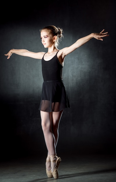 Ballerina. Cute little girl posing and dancing in studio. A little dancer. DarkwallBlack dress.