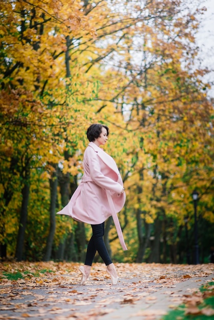 Ballerina dancing in nature among autumn leaves in fair coat.