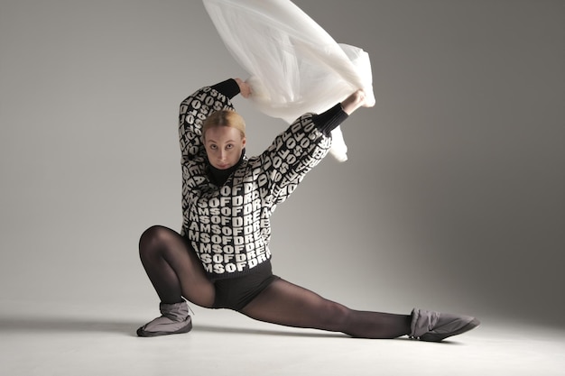 실크 직물로 춤을 추는 발레리나 스웨터에 텍스트가 있는 흰색 직물 회색 배경을 흔들며 현대 발레 댄서