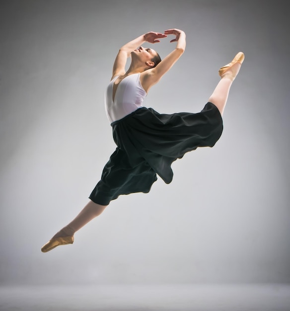 Ballerina full shot standing in pointe shoes jumping with black skirt and white body.