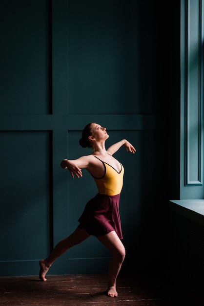 Ballerina in donkere bodysuit, in jurk in donker interieur Studio.